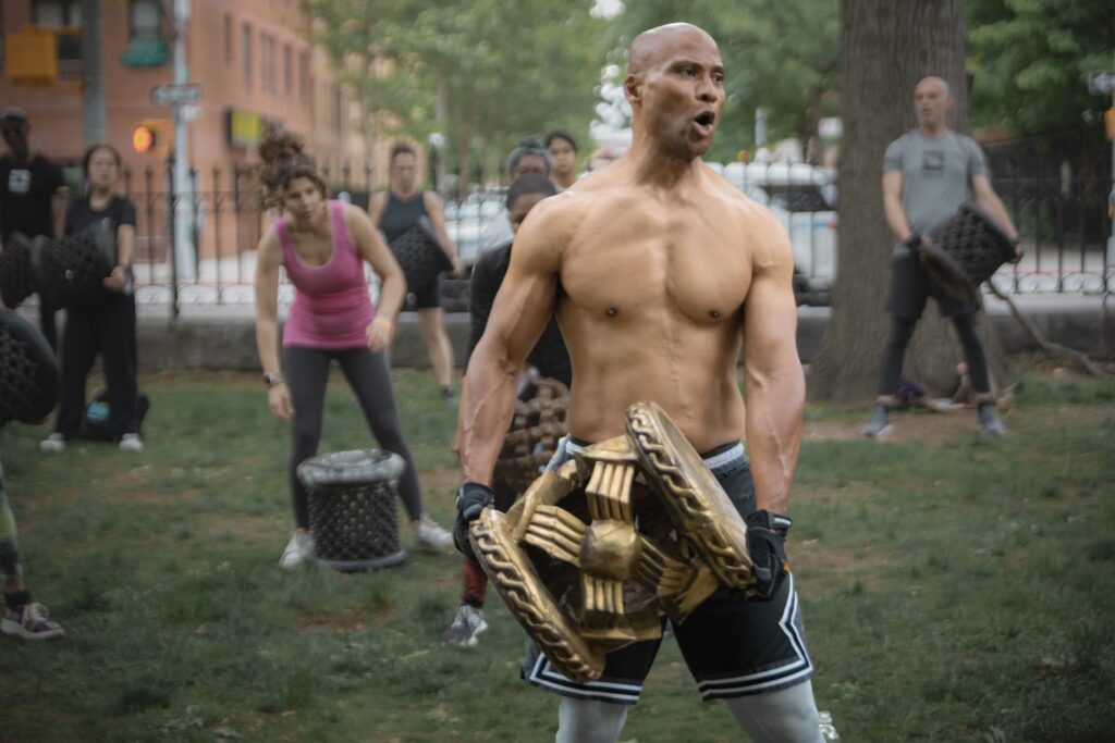 Milton Washington leading a Rokmil Fitness outdoor class while holding the African Rok stool, with participants training behind him.